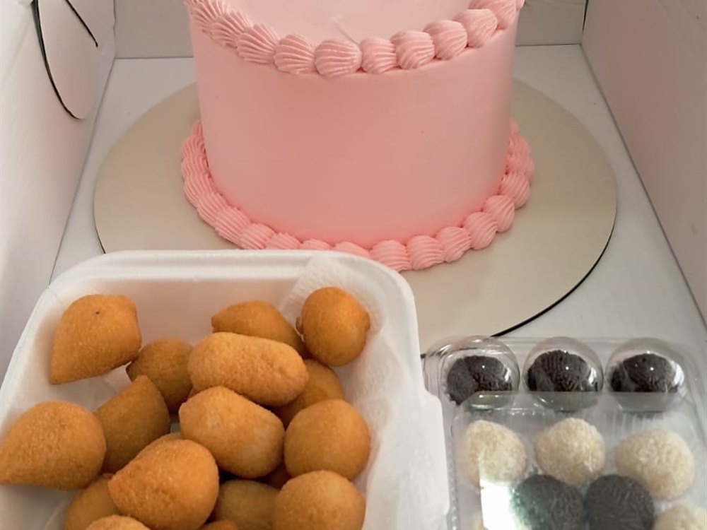 Bolo rosa ao lado de coxinhas, brigadeiros e beijinhos
